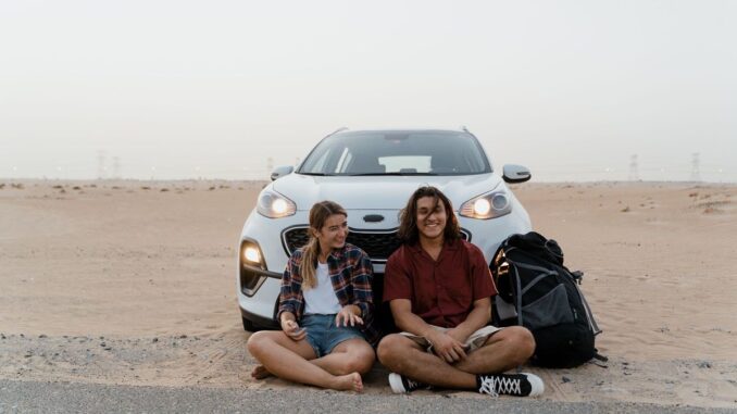 Couple sitting in front of car on road trip