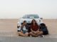 Couple sitting in front of car on road trip